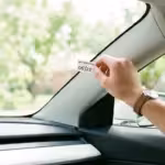 A person attaches a service reminder sticker to the windshield inside a vehicle.