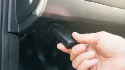 Close-up of a hand connecting a black OBD-II device into a vehicle's diagnostic port.