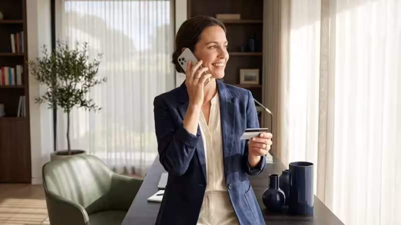 A confident woman in a modern office talking on the phone while holding a credit card, symbolizing successful negotiation.