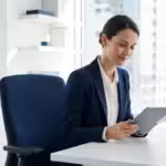 Smiling businesswoman in a navy blazer using a tablet at a modern office desk